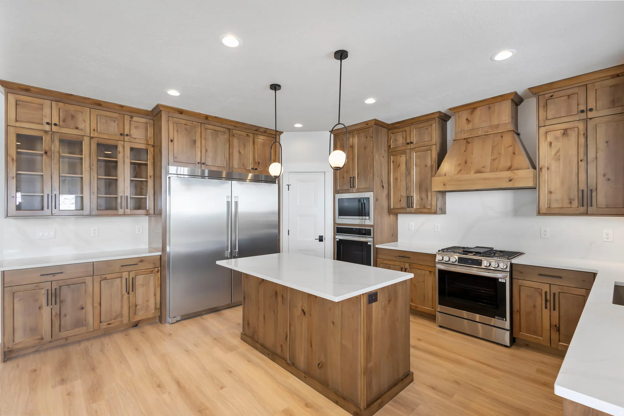 Kitchen featuring built in appliances, wood finish cabinetry, pendant lighting, and glass fronted cabinets