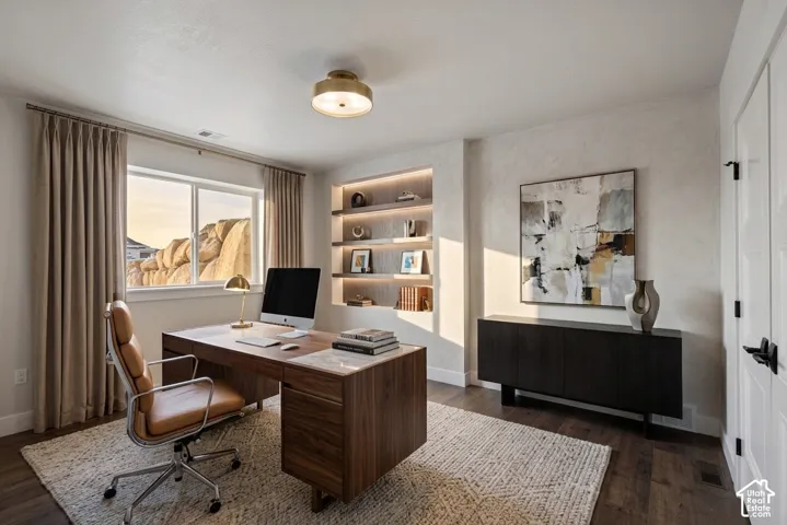Window with exterior rock formation scenery, recessed built-in shelving with integrated lighting, wood-finish flooring, ceiling-mounted light fixture, and a paneled interior door with matte black hardware