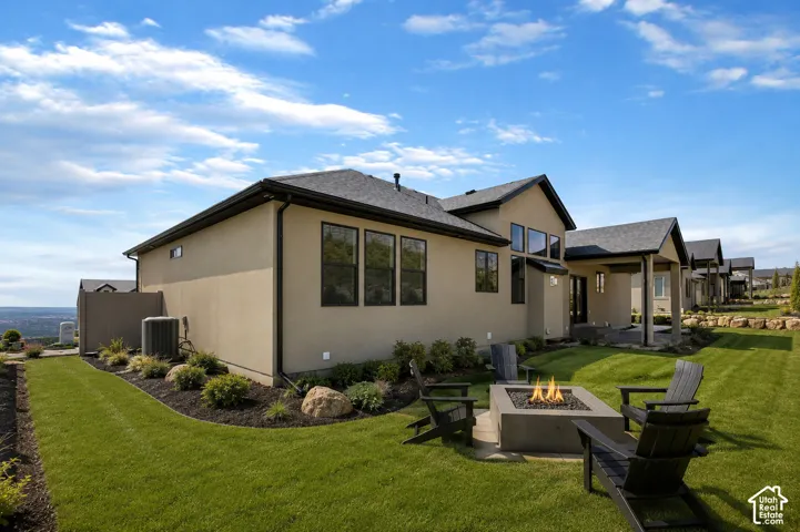 Rear exterior featuring a built-in fire pit, covered patio, manicured lawn, and multiple windows