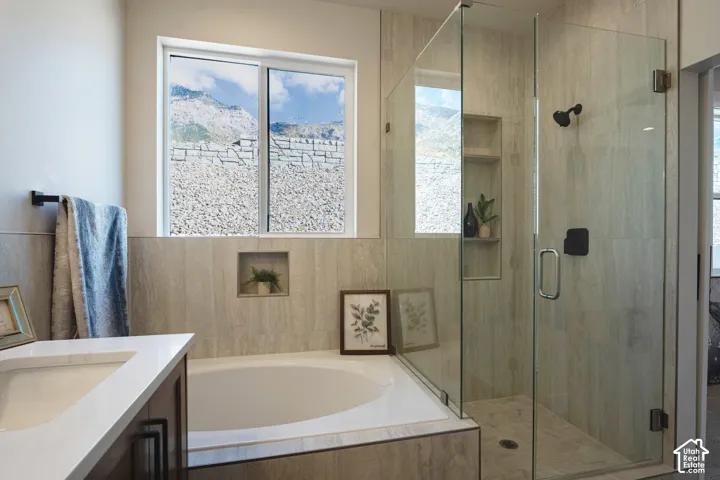 Integrated soaking tub, glass-enclosed shower with tiled walls, built-in shower niche, and a vanity with an integrated sink
