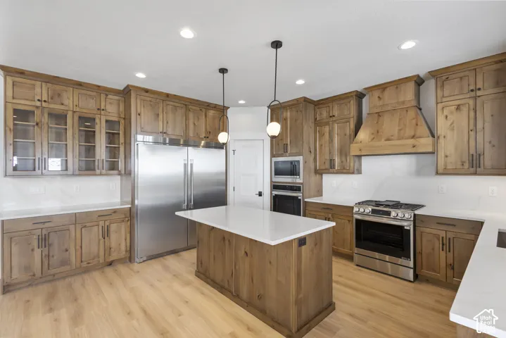 Kitchen featuring built in appliances, wood finish cabinetry, pendant lighting, and glass fronted cabinets