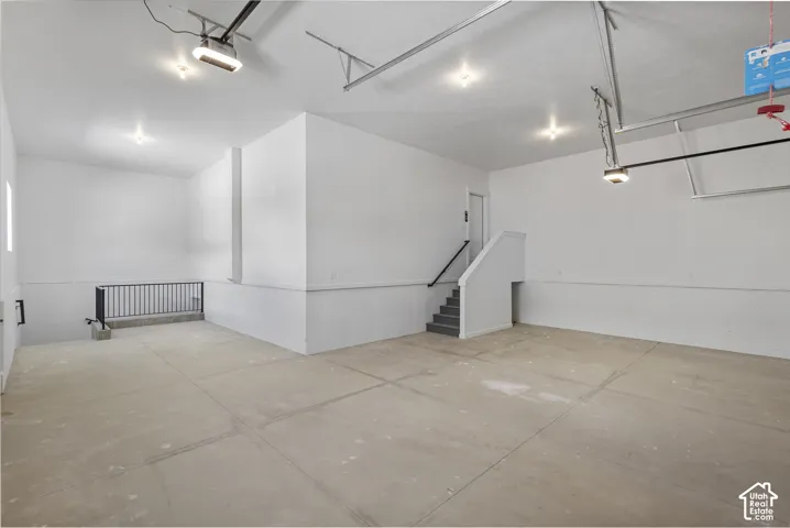 Spacious garage featuring a concrete floor, bright overhead lighting, painted walls, and an interior staircase with a handrail