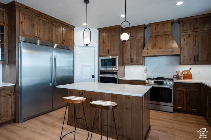 Wood-finish cabinetry with black hardware, stainless steel appliances, kitchen island with solid surface countertop, wood-finish flooring, and recessed lighting