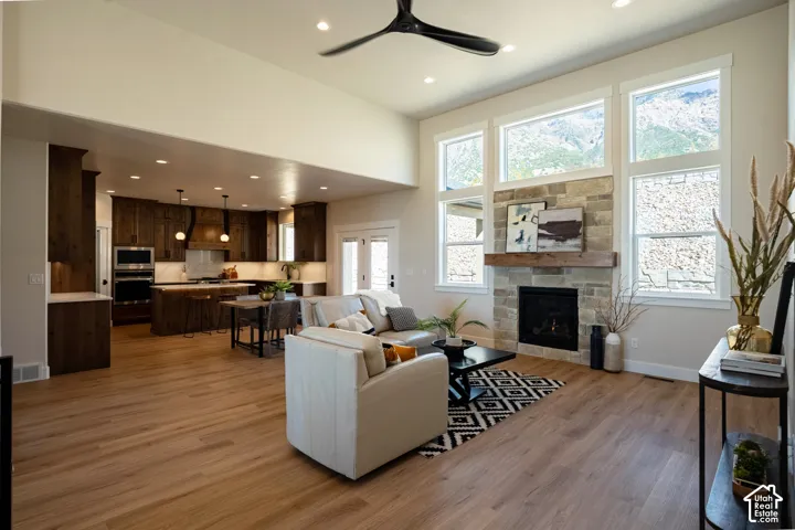 Spacious open-concept living area featuring wood-finish flooring, a stone-surround fireplace with a wood mantel, and expansive windows