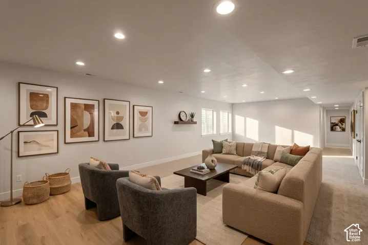 Recessed ceiling lighting illuminates a spacious room featuring wood-finish flooring, multiple windows, and a built-in floating shelf