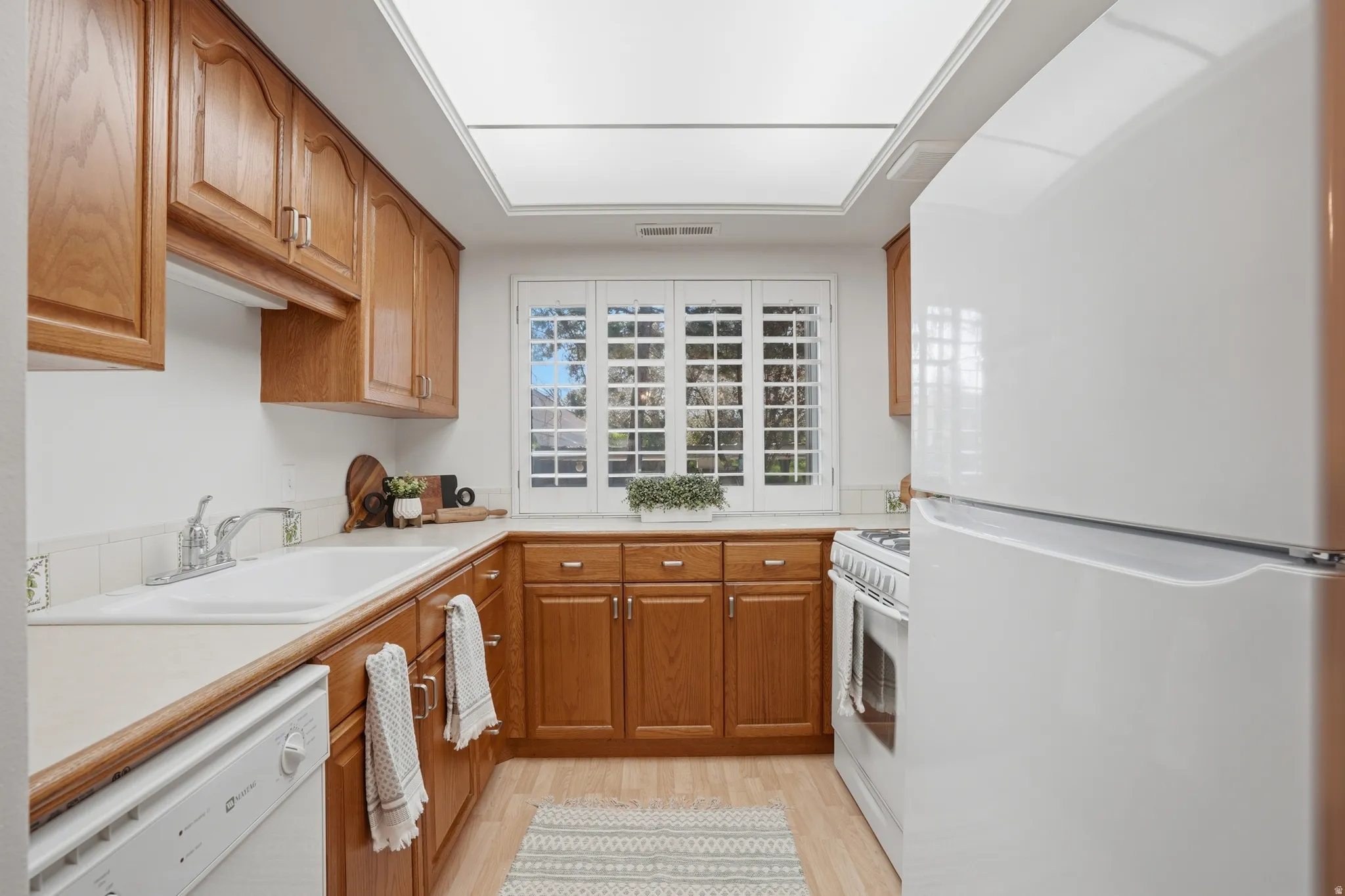 Kitchen featuring white appliances, light countertops, wood finish cabinets, and light wood-style floors