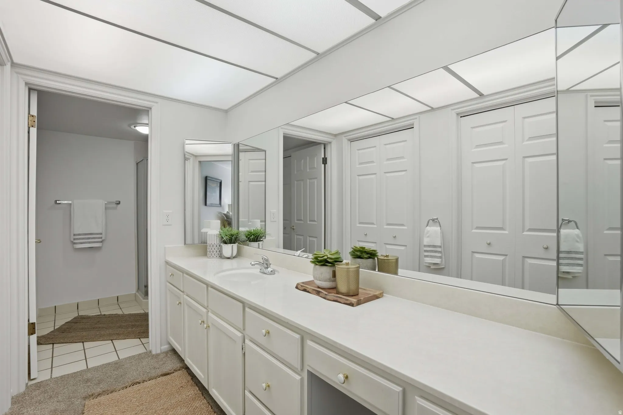 Bathroom featuring a closet, vanity, light tile patterned flooring, and a stall shower