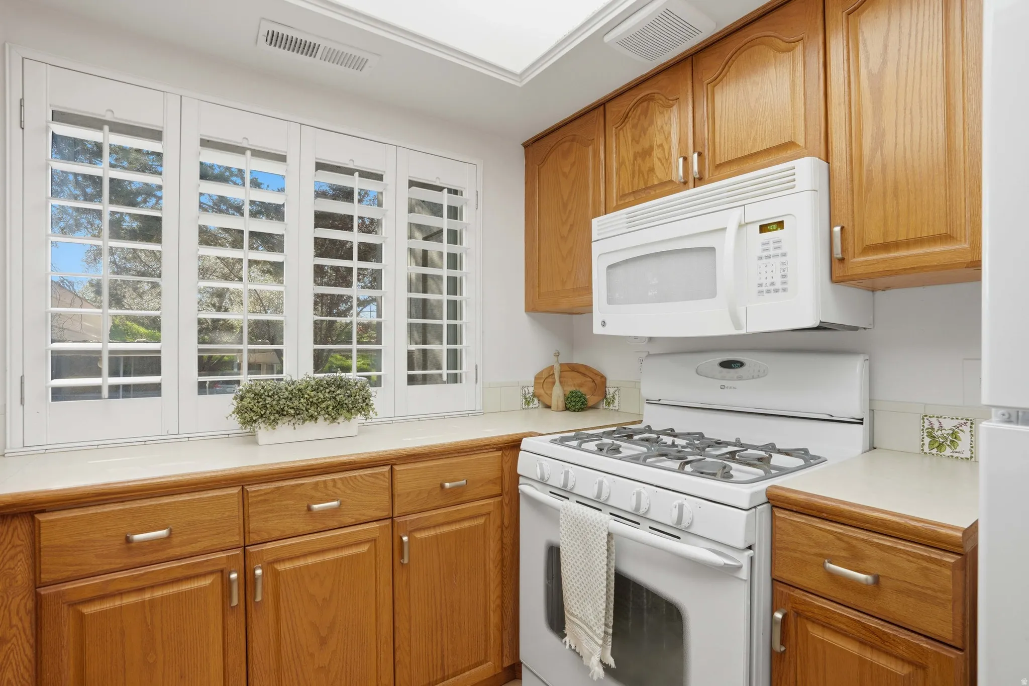 Kitchen with white appliances, light countertops, and wood finish cabinetry