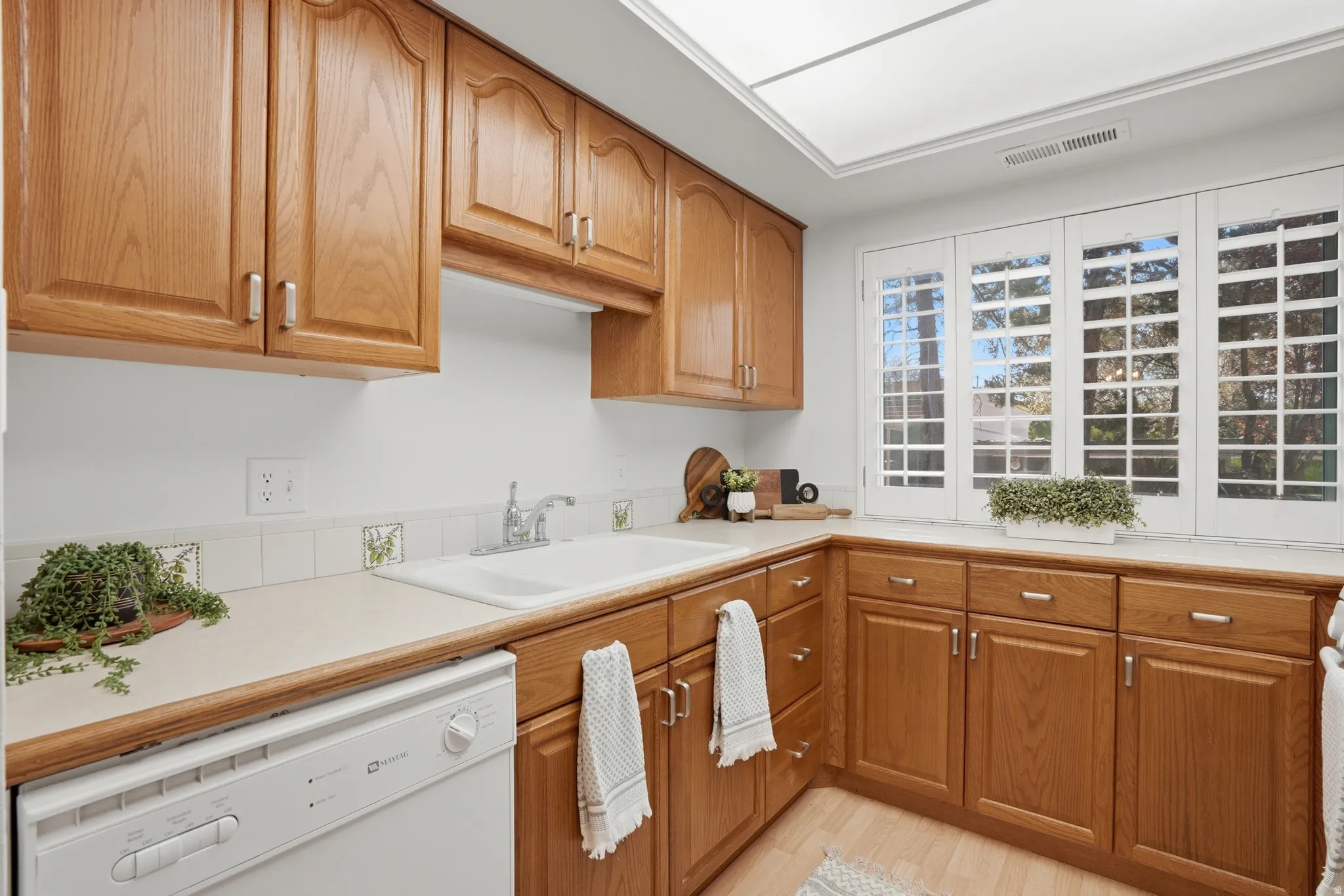 Kitchen featuring white dishwasher, light countertops, wood finish cabinetry, and light wood finished floors
