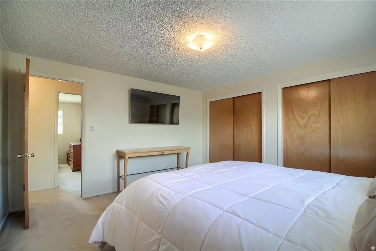 Bedroom with a textured ceiling, multiple closets, and carpet floors