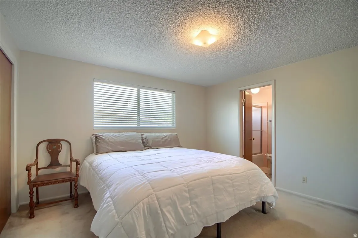 Bedroom with light colored carpet, a textured ceiling, a closet, and connected bathroom