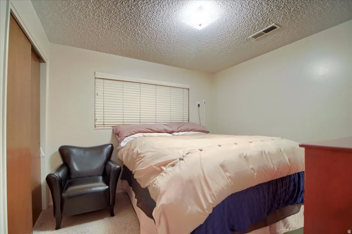 Carpeted bedroom featuring a textured ceiling and a closet
