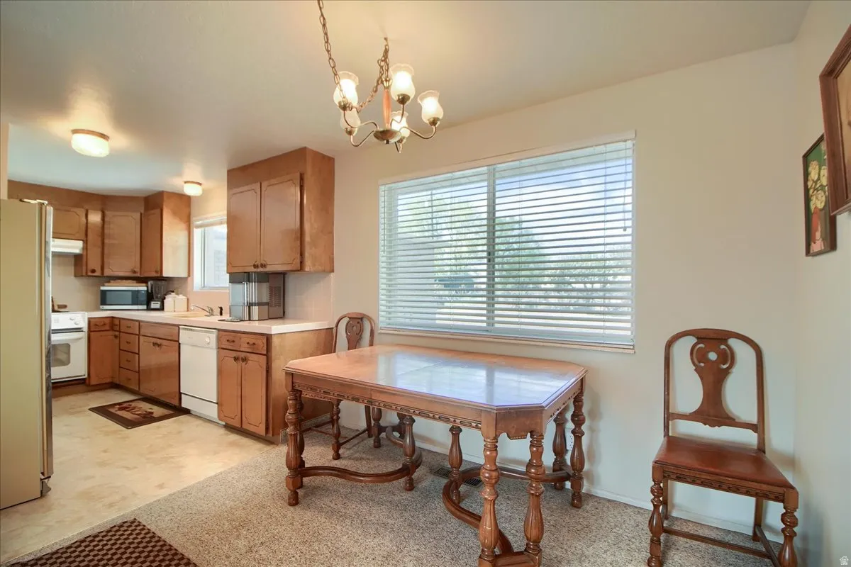 Kitchen featuring white appliances, wood finish cabinetry, a chandelier, and light countertops