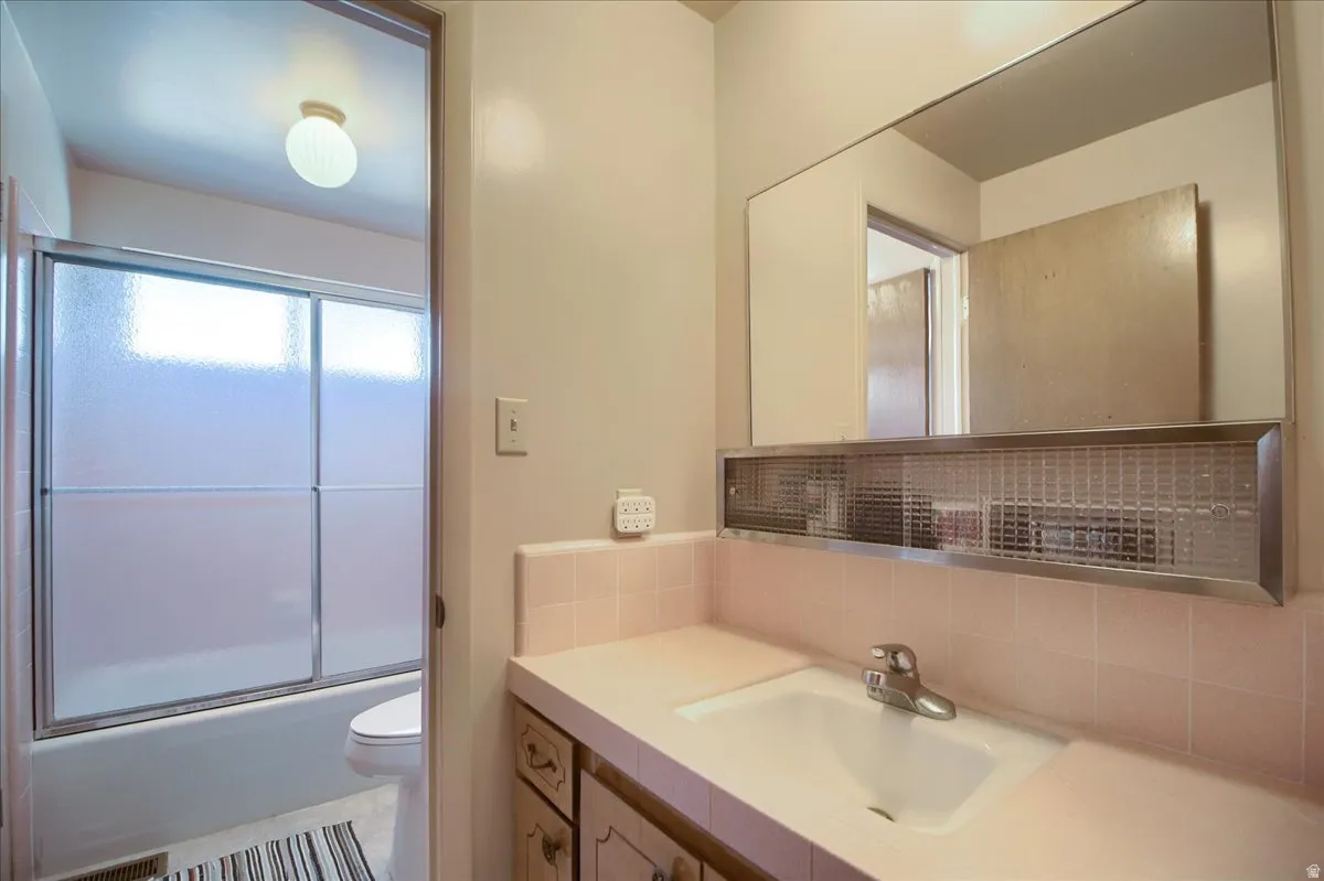 Bathroom featuring vanity, tasteful backsplash, and enclosed tub / shower combo