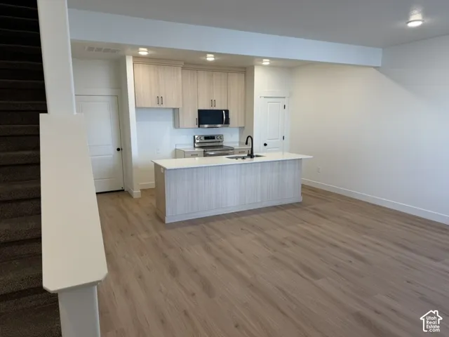 Kitchen with stainless steel appliances, light wood-type flooring, an island with sink, light wood finish cabinets, and recessed lighting