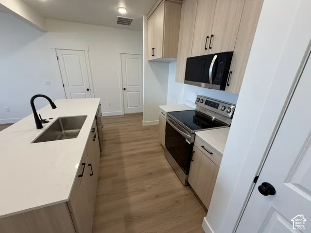 Kitchen featuring light wood finish cabinets, stainless steel appliances, light wood-style floors, and a center island with sink
