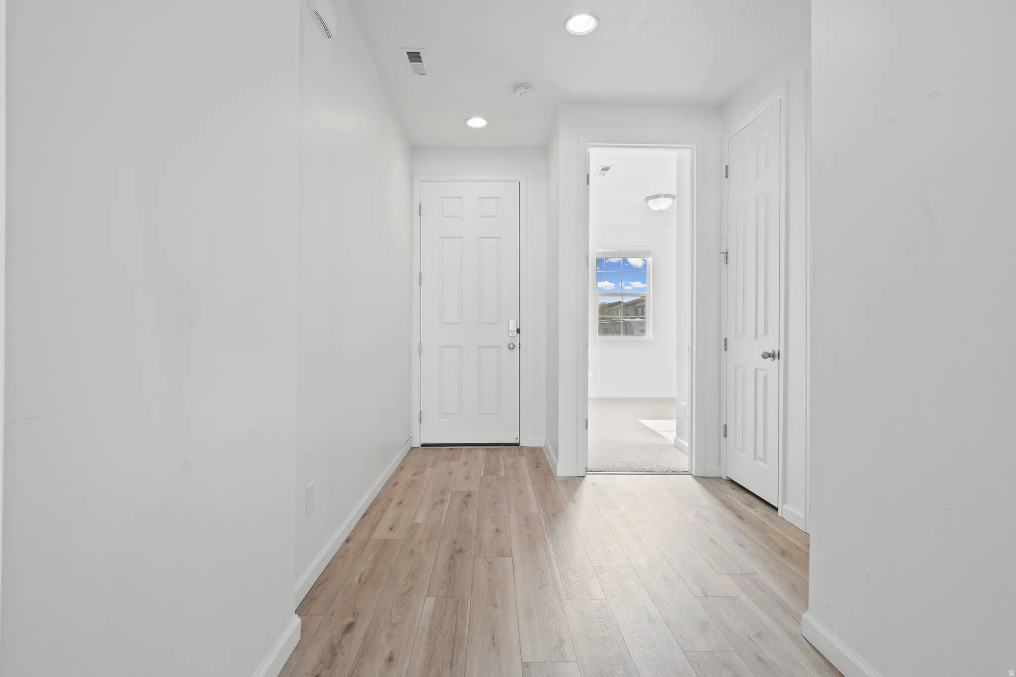 Entryway featuring wood-finish flooring, white paneled doors, recessed lighting, and white baseboards