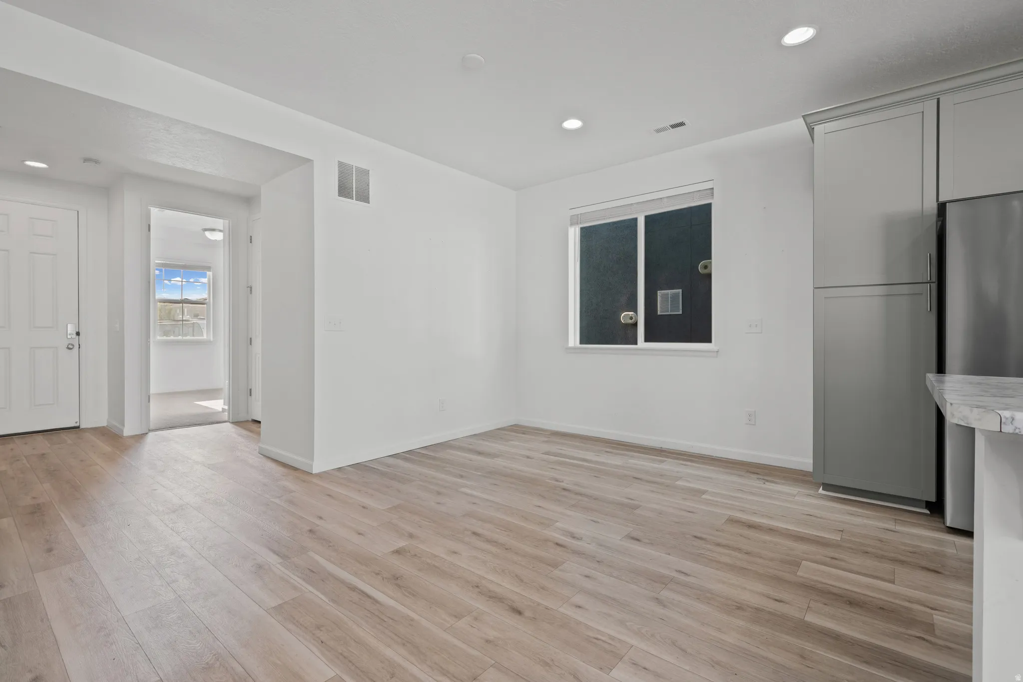 Open-concept living space with light-toned wood-finish flooring, recessed lighting, and white walls
