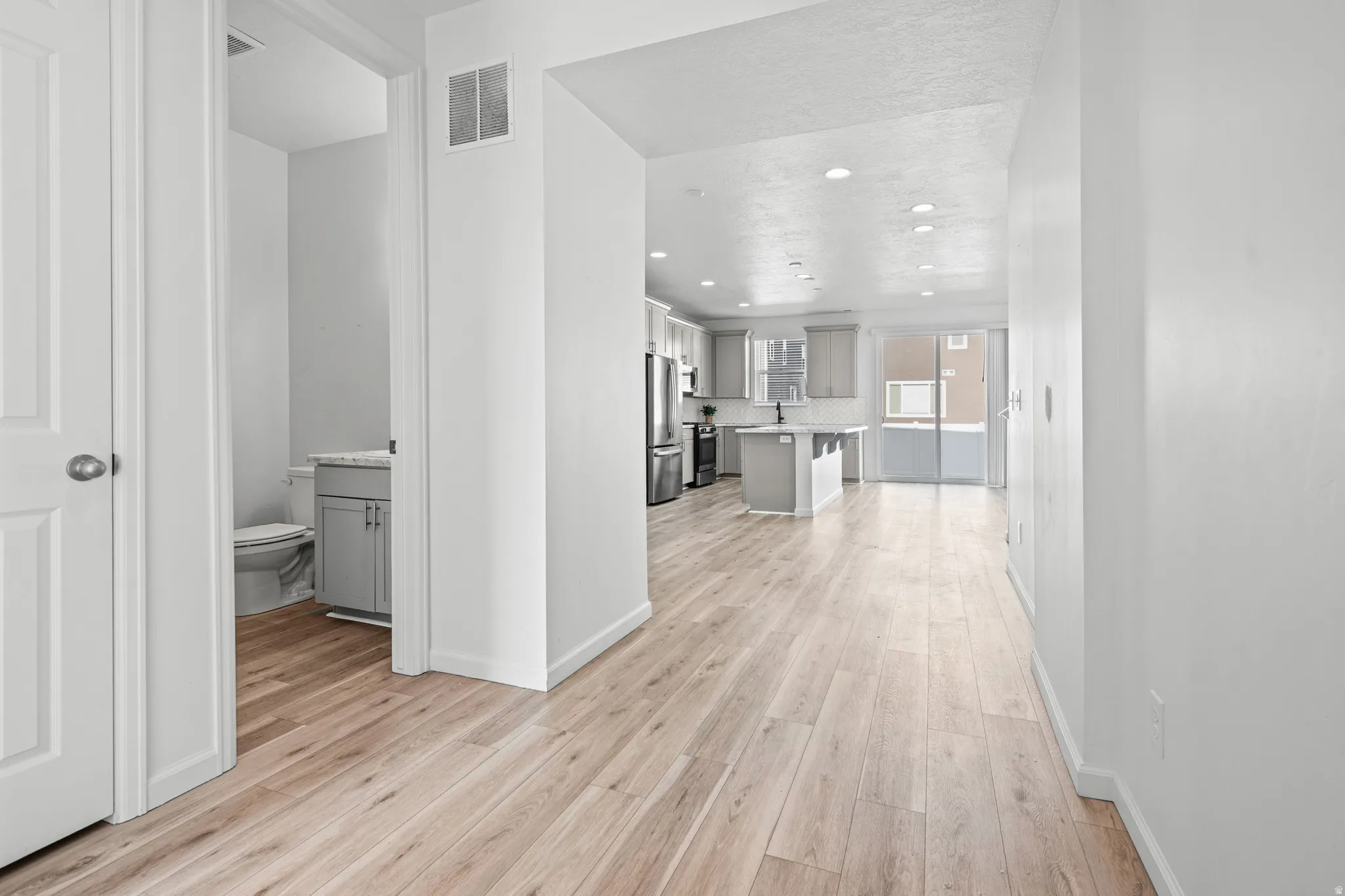 Spacious interior featuring light wood-finish flooring, recessed lighting, a modern kitchen with gray cabinetry, and sliding glass doors