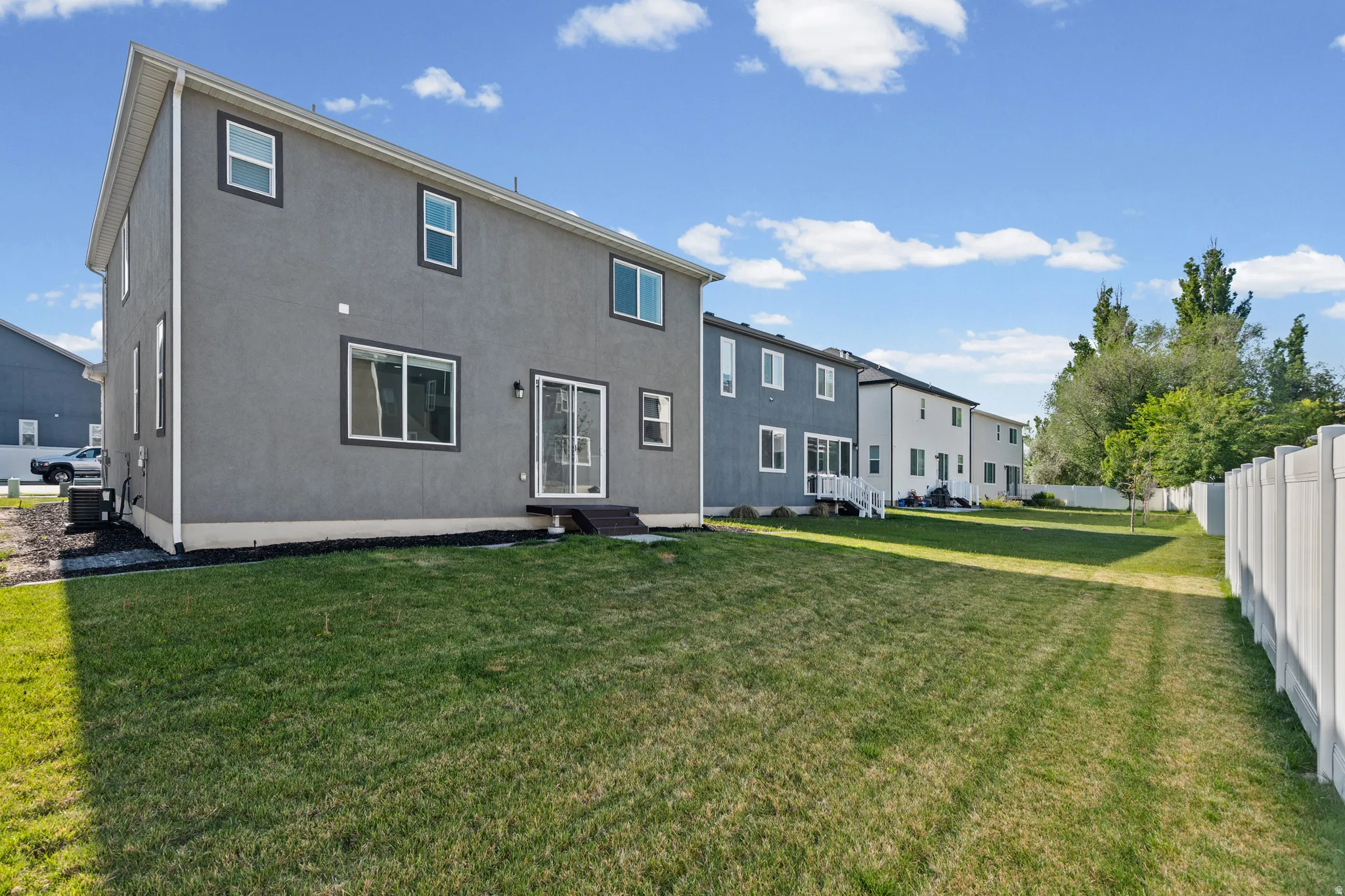 Spacious rear yard with a manicured lawn, vinyl privacy fencing, and mature trees