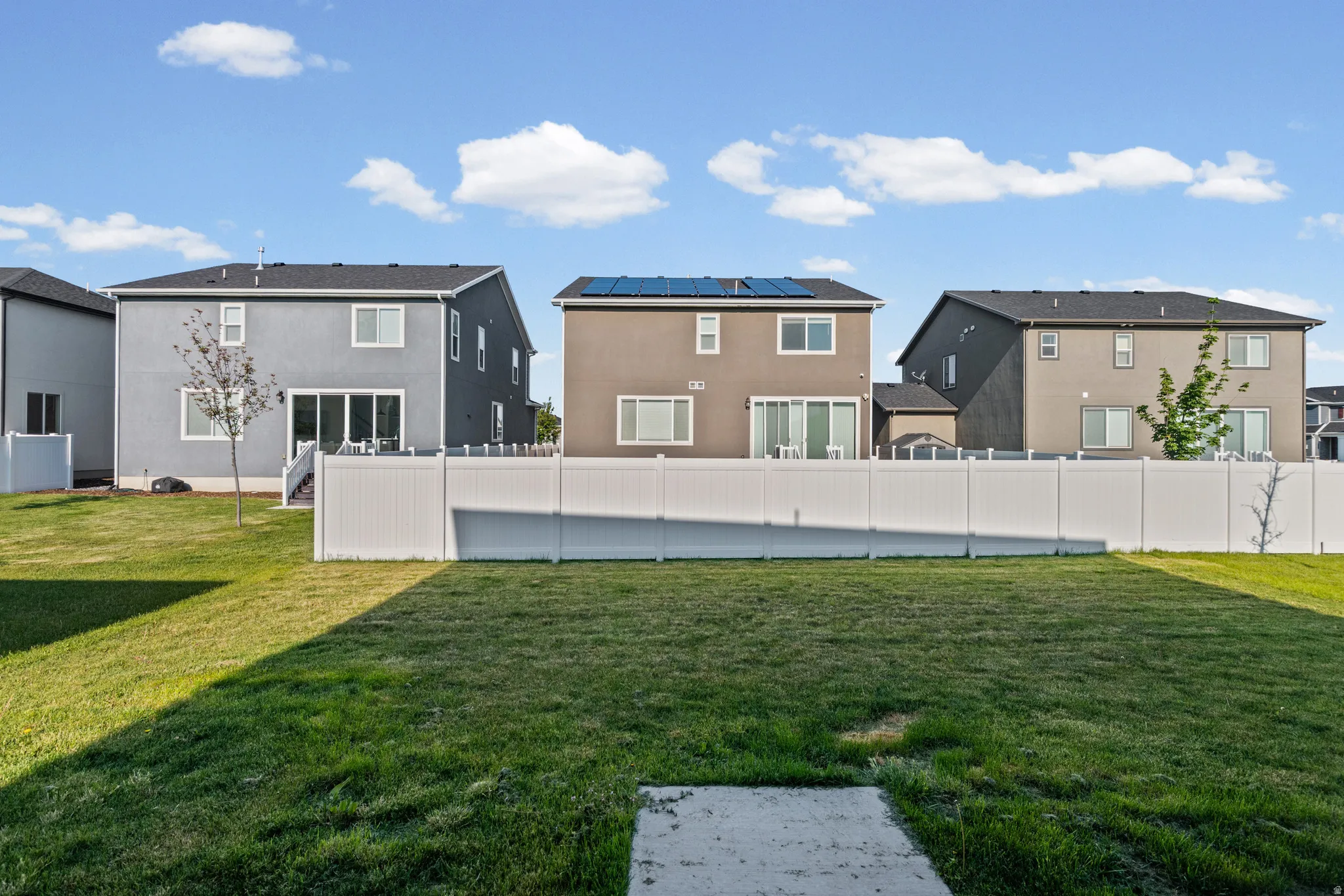 Expansive backyard featuring a manicured lawn, a concrete pad, and a full-height white vinyl fence