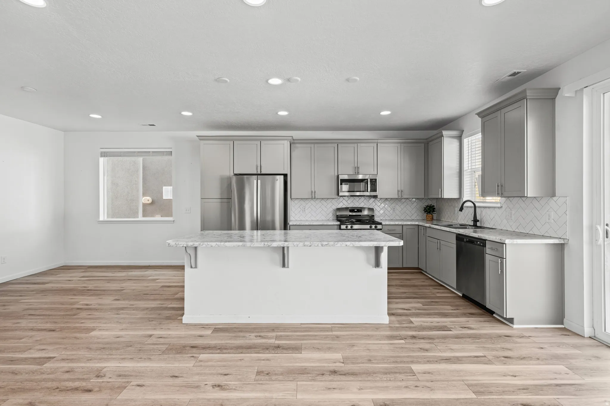 Kitchen featuring a central island with countertop seating, light gray cabinetry, stainless steel appliances, and a white herringbone tile backsplash