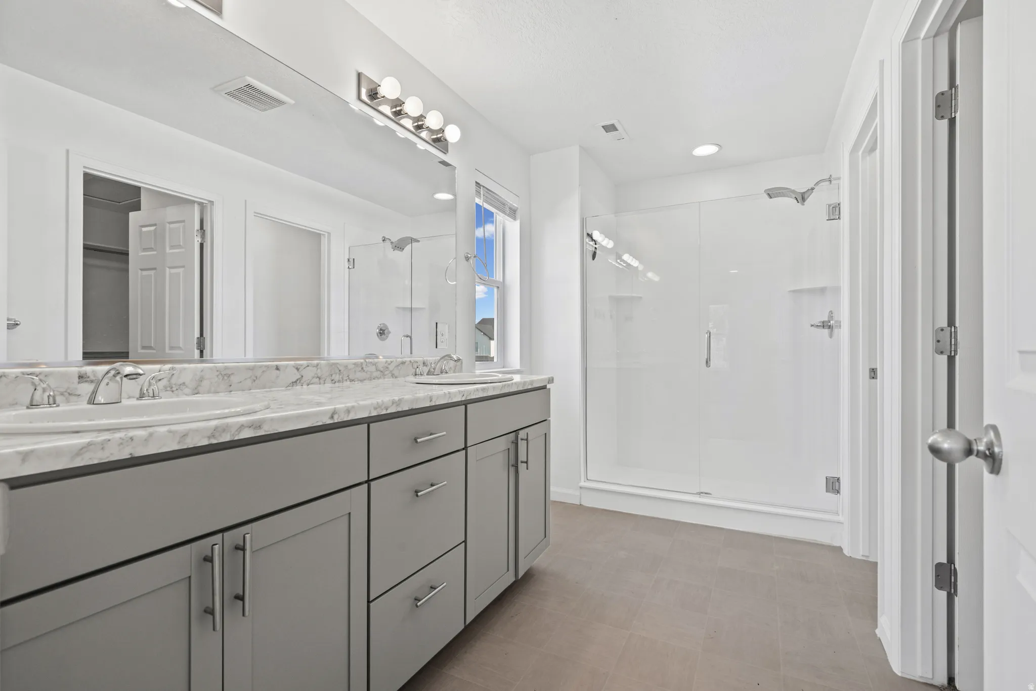 Spacious bathroom featuring a double vanity with grey cabinetry, a patterned countertop, and dual undermount sinks