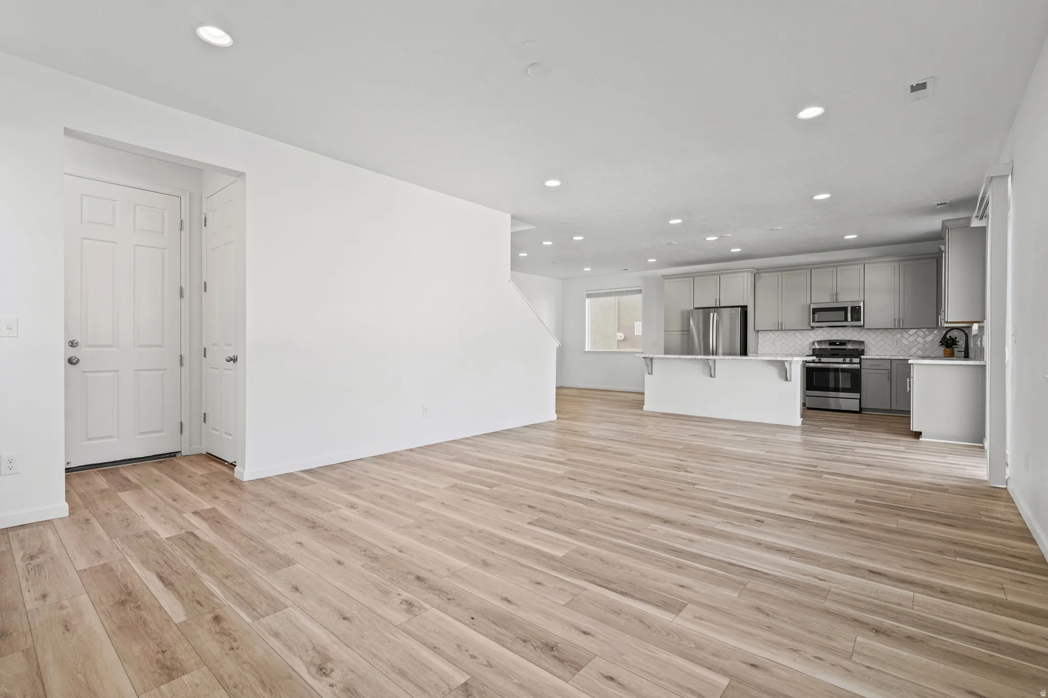 Open-concept living area featuring wood-finish flooring, recessed lighting, and a kitchen with stainless steel appliances