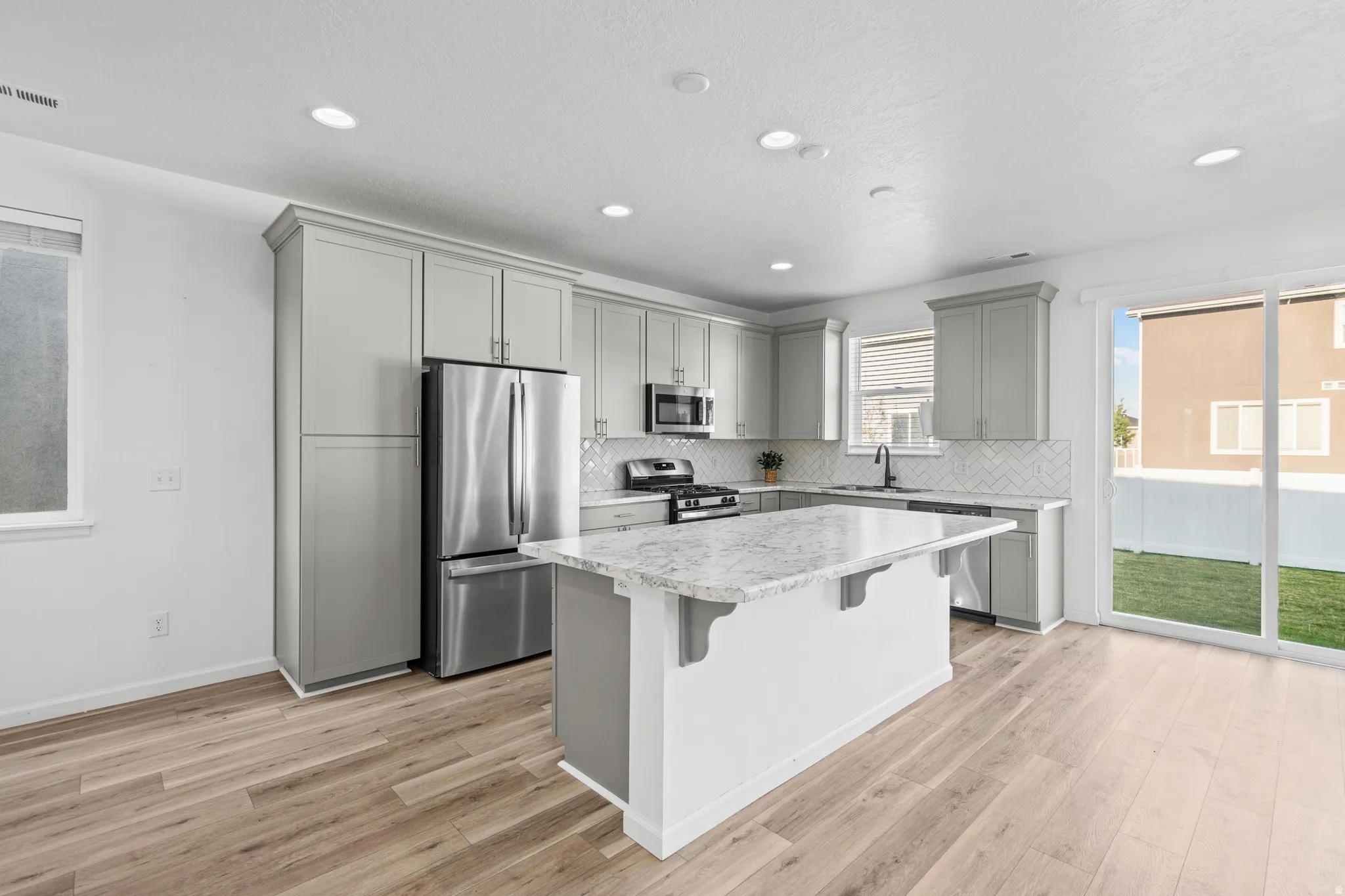 Modern kitchen featuring light gray cabinetry, stainless steel appliances, a center island with a stone countertop, and wood-finish flooring