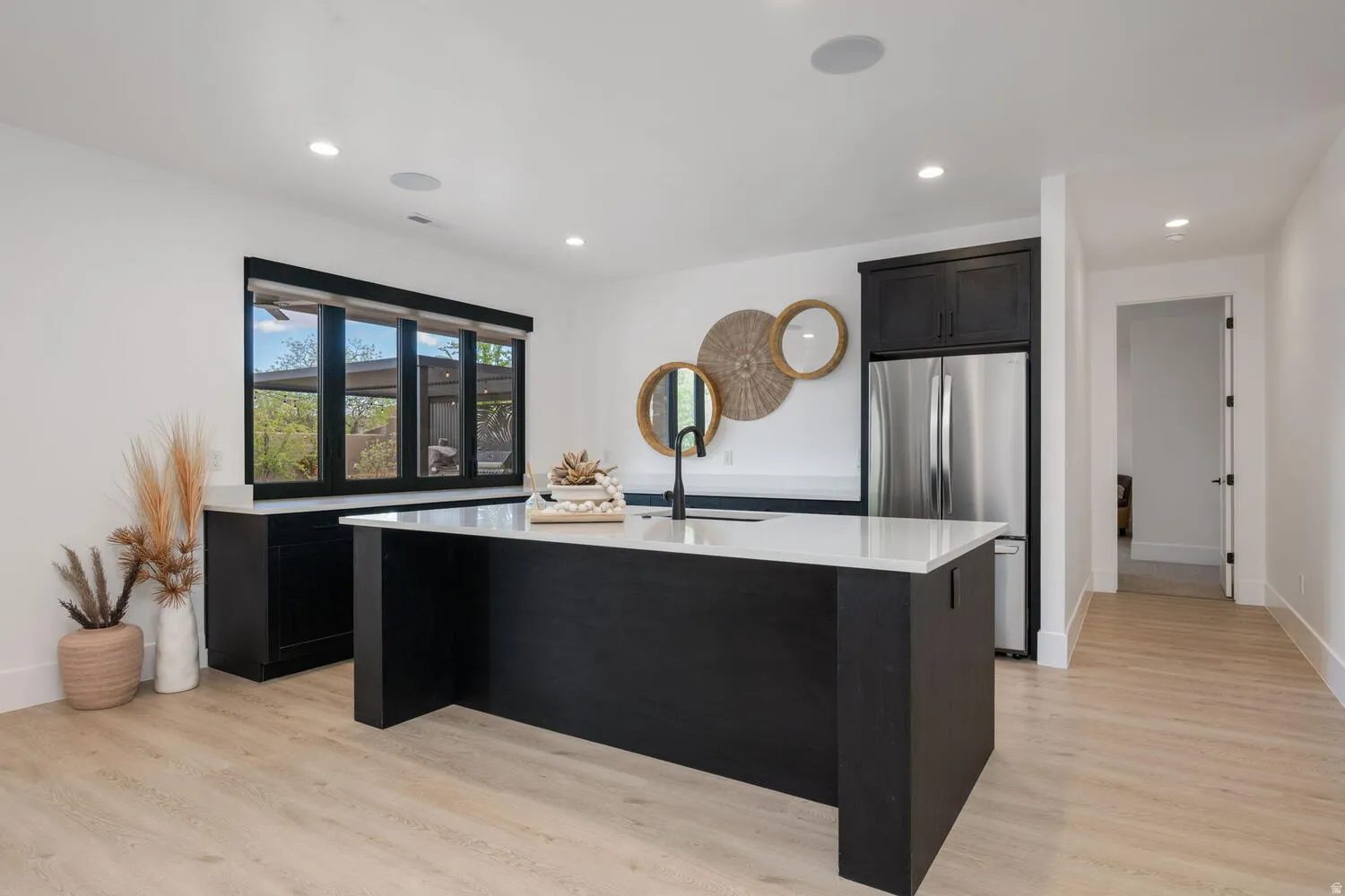 Kitchen featuring an island with sink, freestanding refrigerator, dark cabinets, light wood-style floors, and recessed lighting