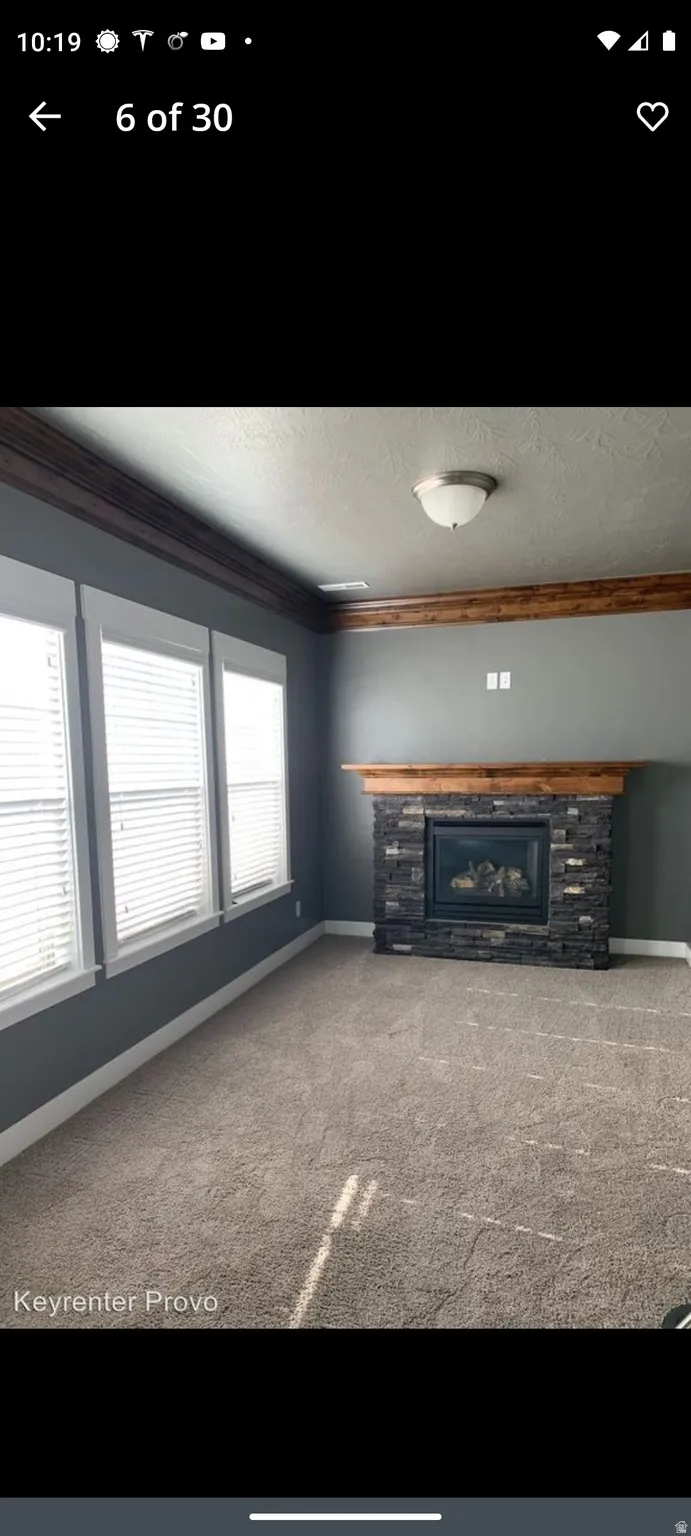 Unfurnished living room featuring crown molding, a fireplace, carpet floors, and a textured ceiling