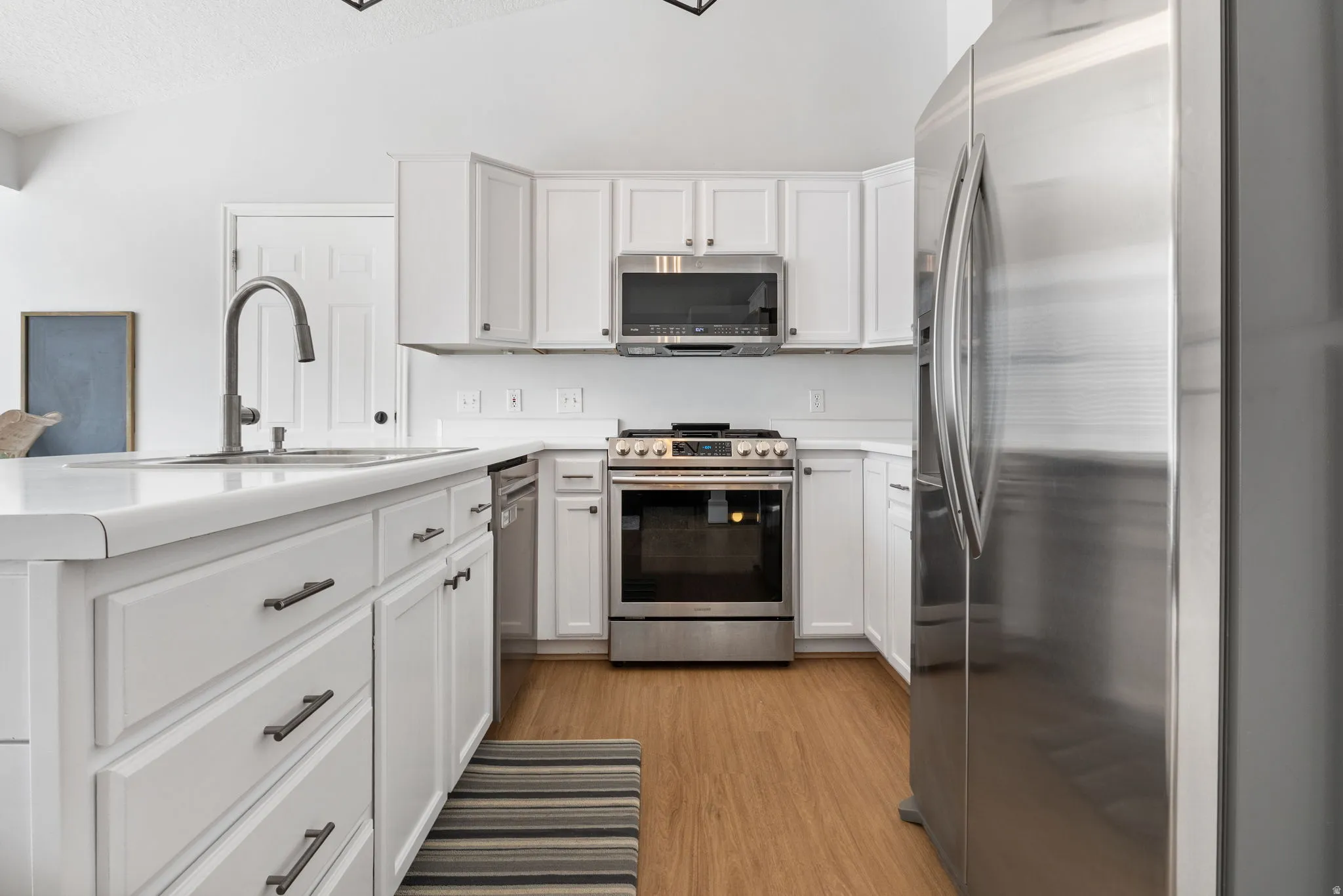 Kitchen featuring stainless steel appliances, light countertops, lofted ceiling, and white cabinetry