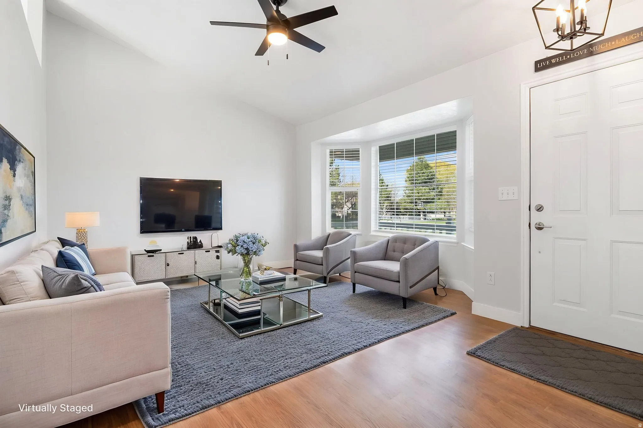 Living room featuring wood finished floors, a ceiling fan, vaulted ceiling, and a chandelier