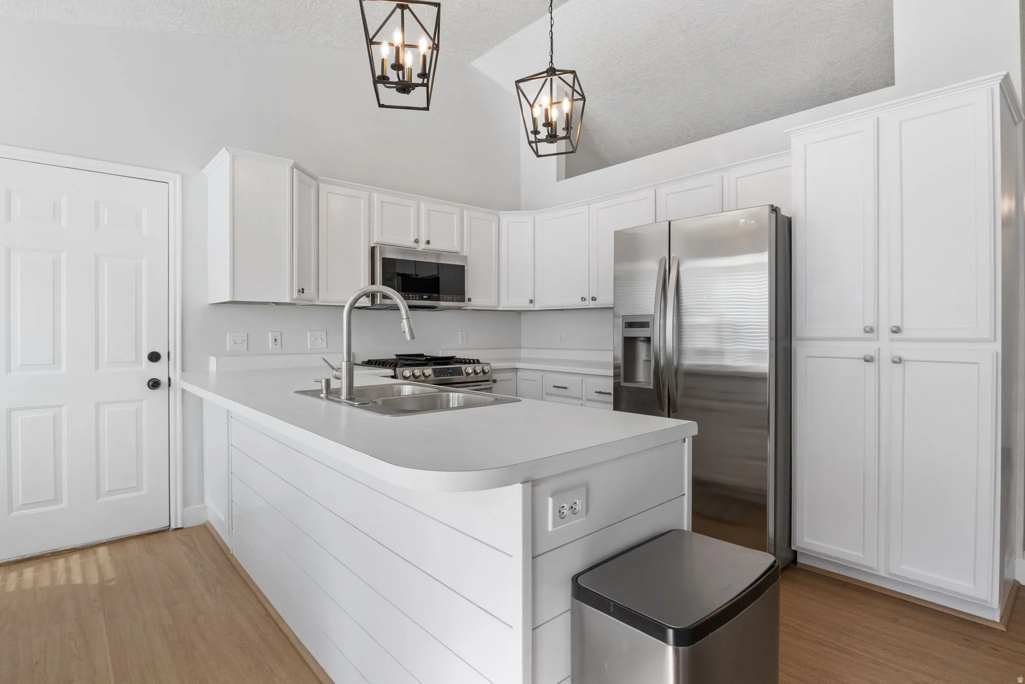 Kitchen featuring stainless steel appliances, white cabinetry, light wood finished floors, and a peninsula