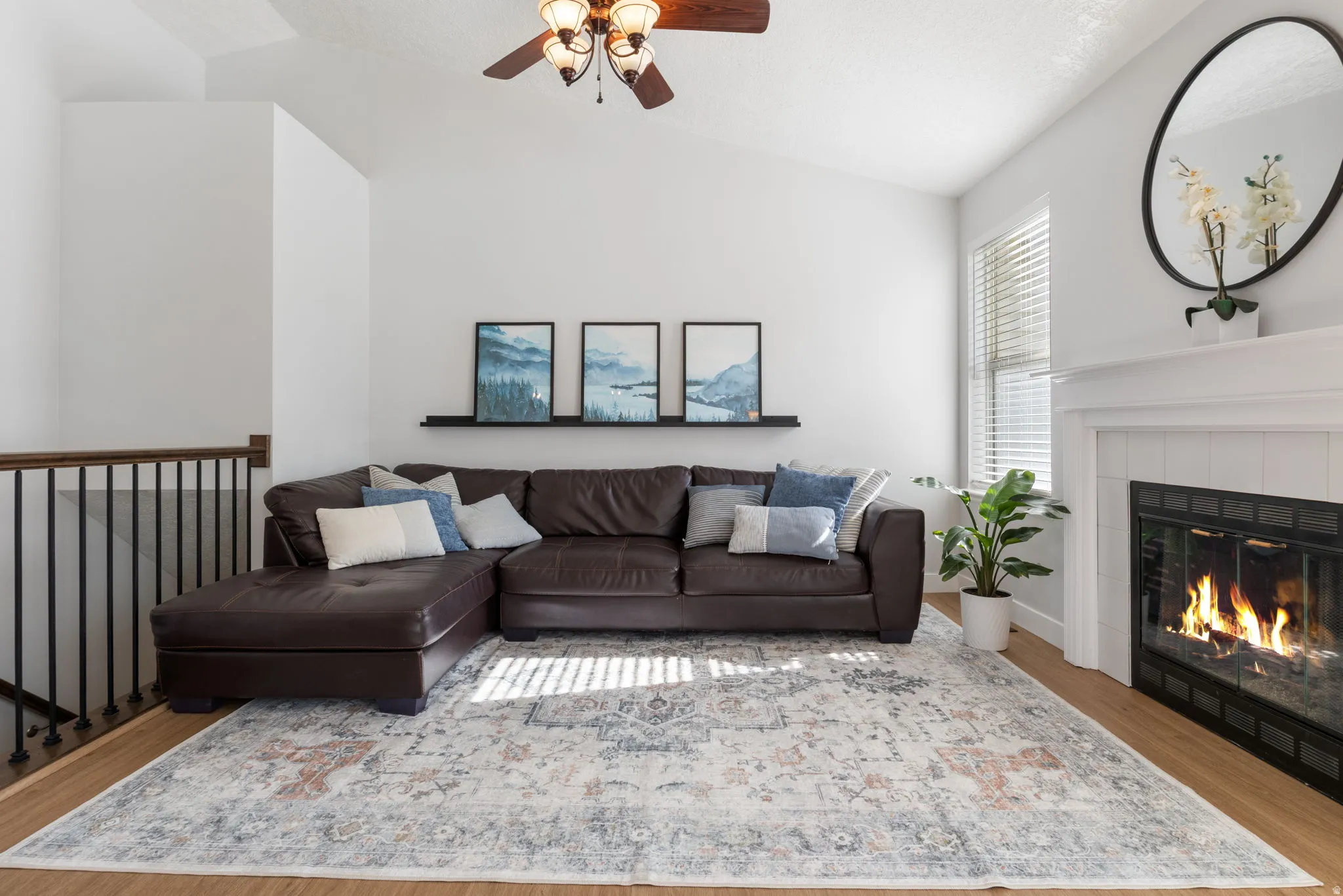 Living room with wood finished floors, lofted ceiling, ceiling fan, and a tiled fireplace