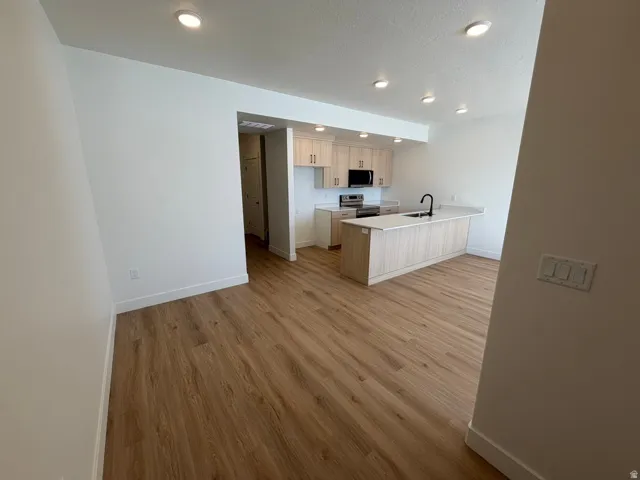 Kitchen featuring a peninsula, light countertops, light wood finished floors, stainless steel range with electric stovetop, and a breakfast bar area