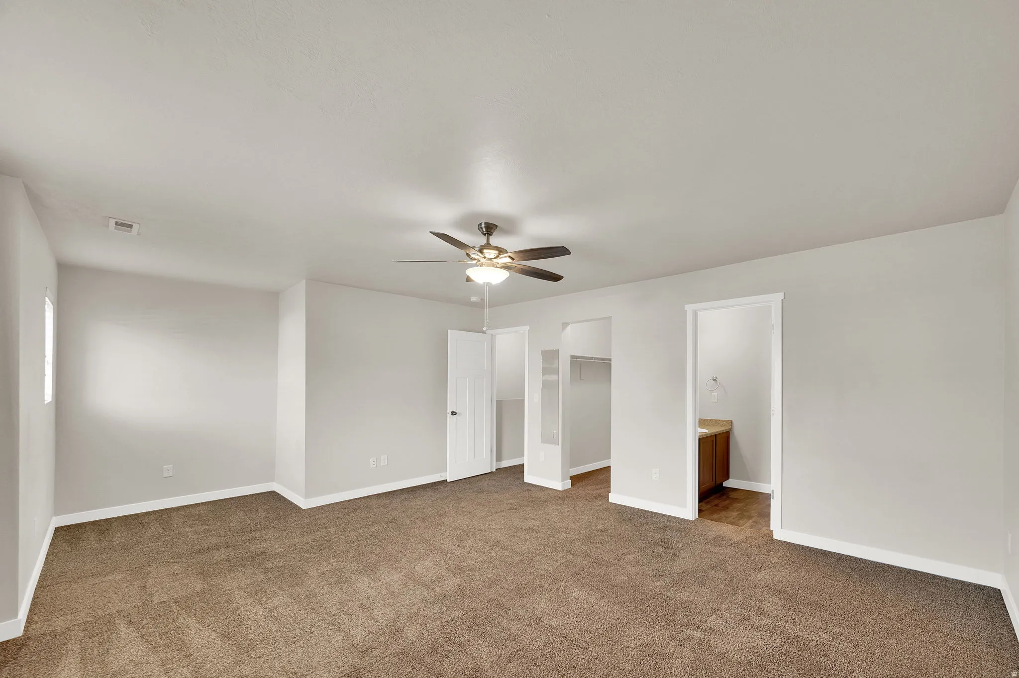 Bedroom with a spacious closet, dark carpet, a ceiling fan, and ensuite bath