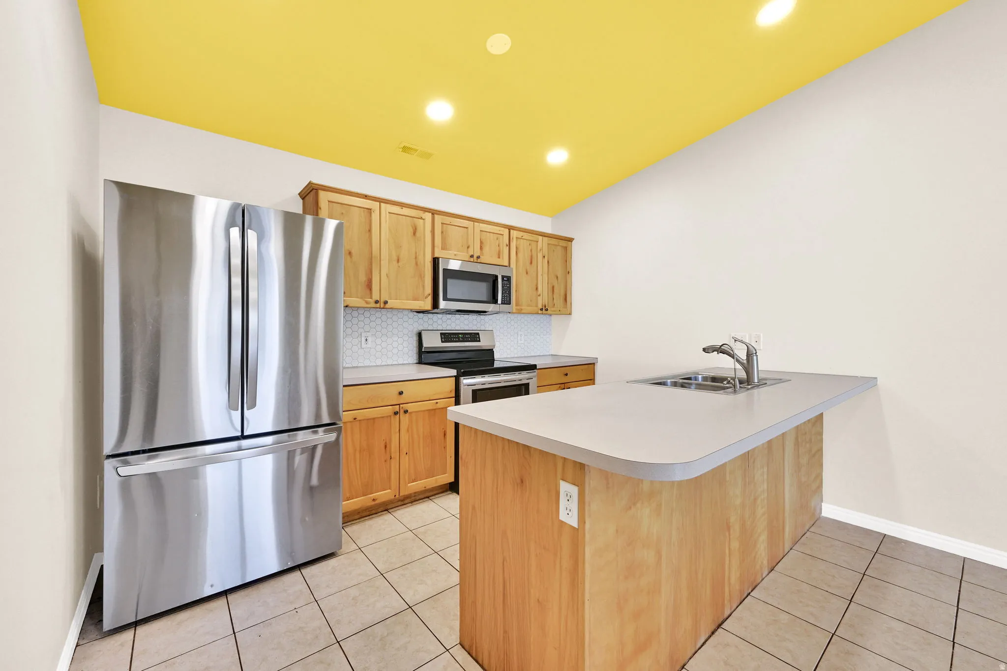 Kitchen with stainless steel appliances, light tile patterned floors, a peninsula, light countertops, and recessed lighting