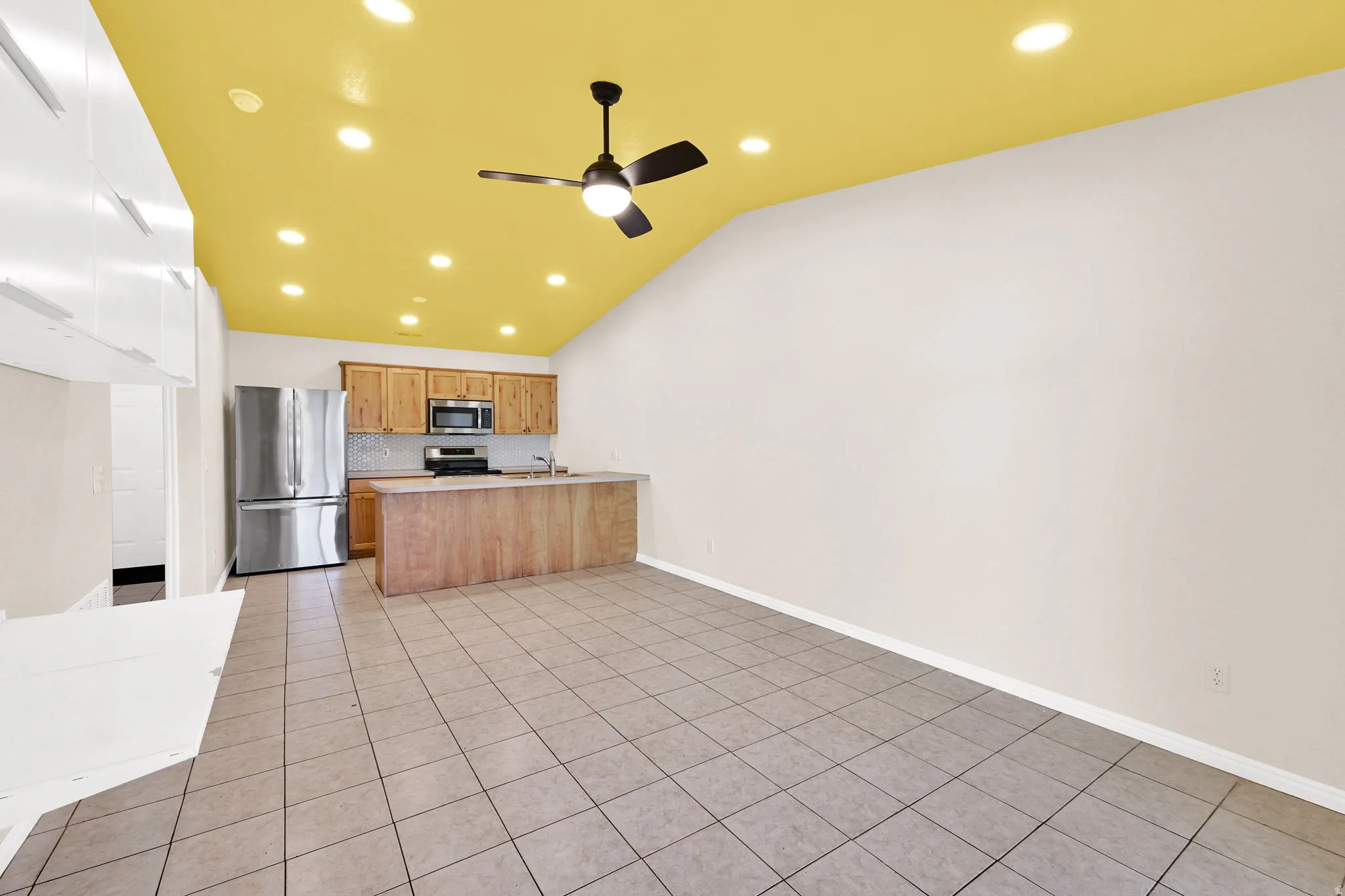 Kitchen with a peninsula, stainless steel appliances, light countertops, light tile patterned floors, and ceiling fan
