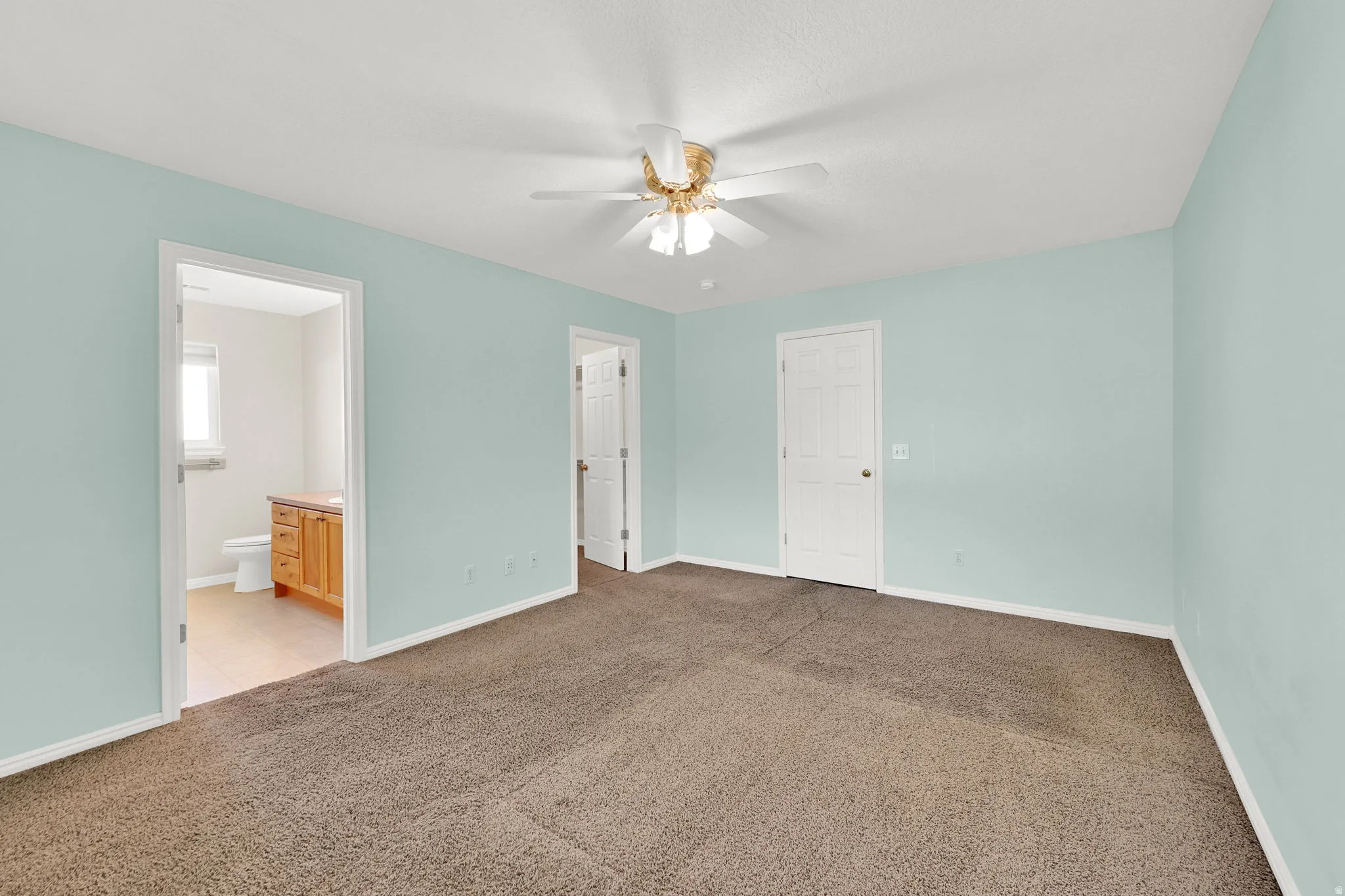 Primary bedroom with light colored carpet, ceiling fan, and ensuite bathroom