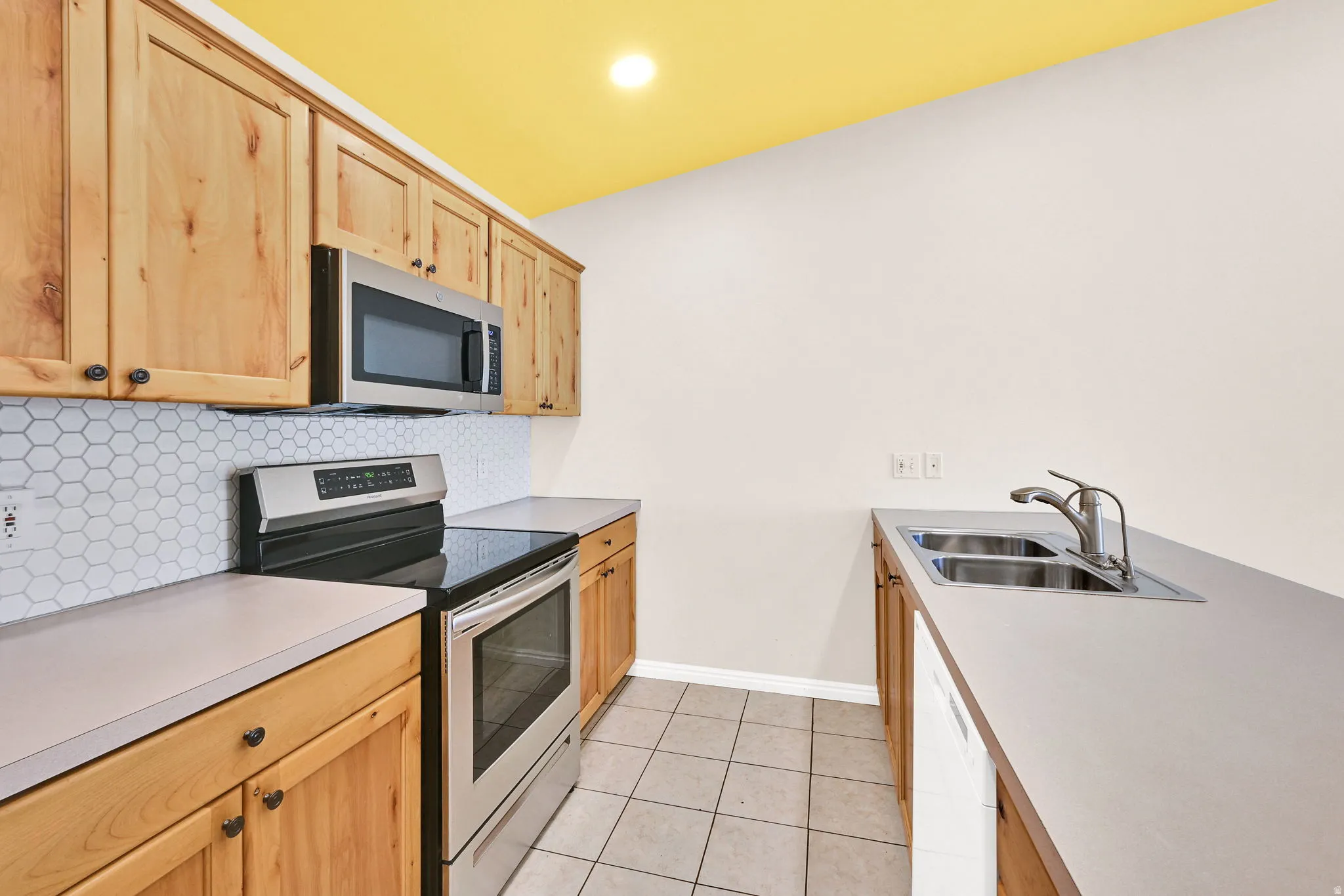 Kitchen with stainless steel appliances, light countertops, light wood finish cabinets, light tile patterned floors, and recessed lighting