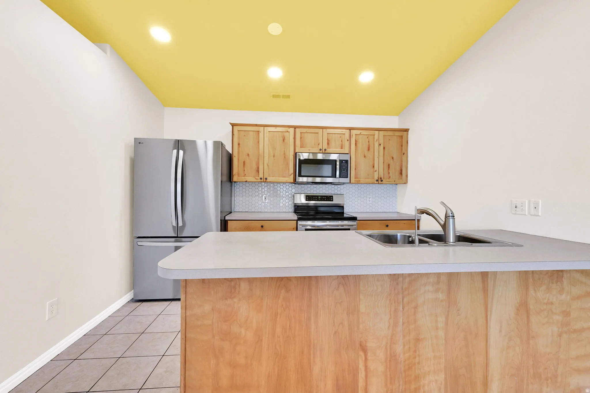 Kitchen with a peninsula, stainless steel appliances, light countertops, backsplash, and light wood finish cabinetry