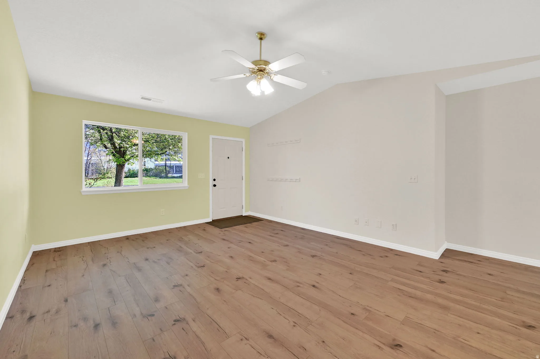 Empty room with light wood-style flooring, lofted ceiling, and a ceiling fan