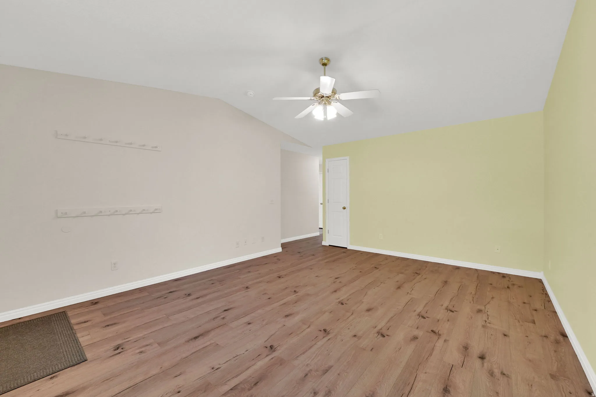 Empty room featuring light wood-style flooring, lofted ceiling, and ceiling fan