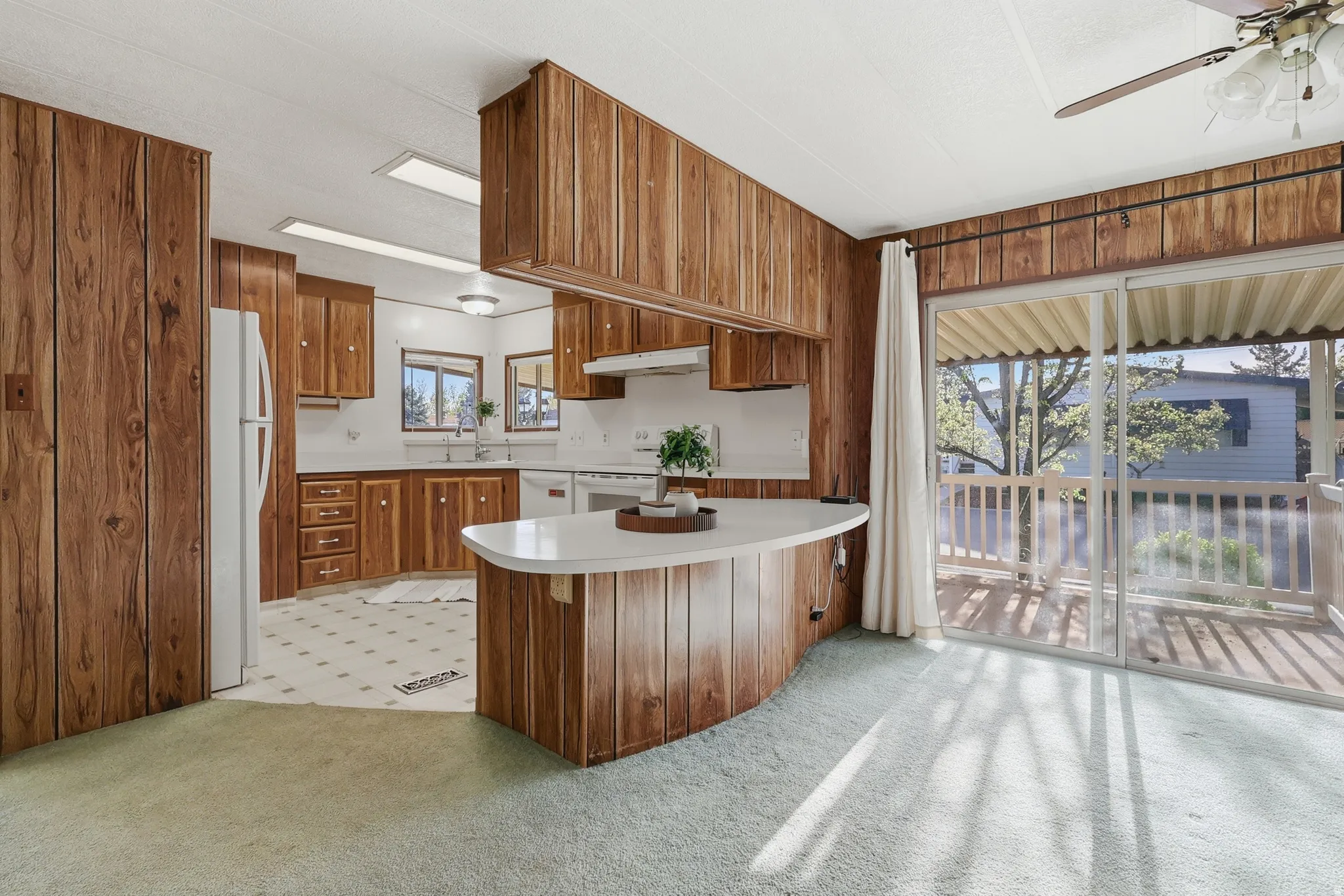 Kitchen featuring light countertops, wood finish cabinetry, wood walls, white appliances, and ceiling fan