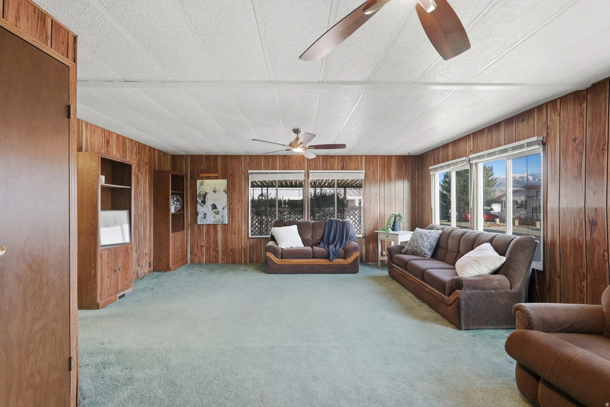 Living room with wooden walls, light carpet, a ceiling fan, and a textured ceiling