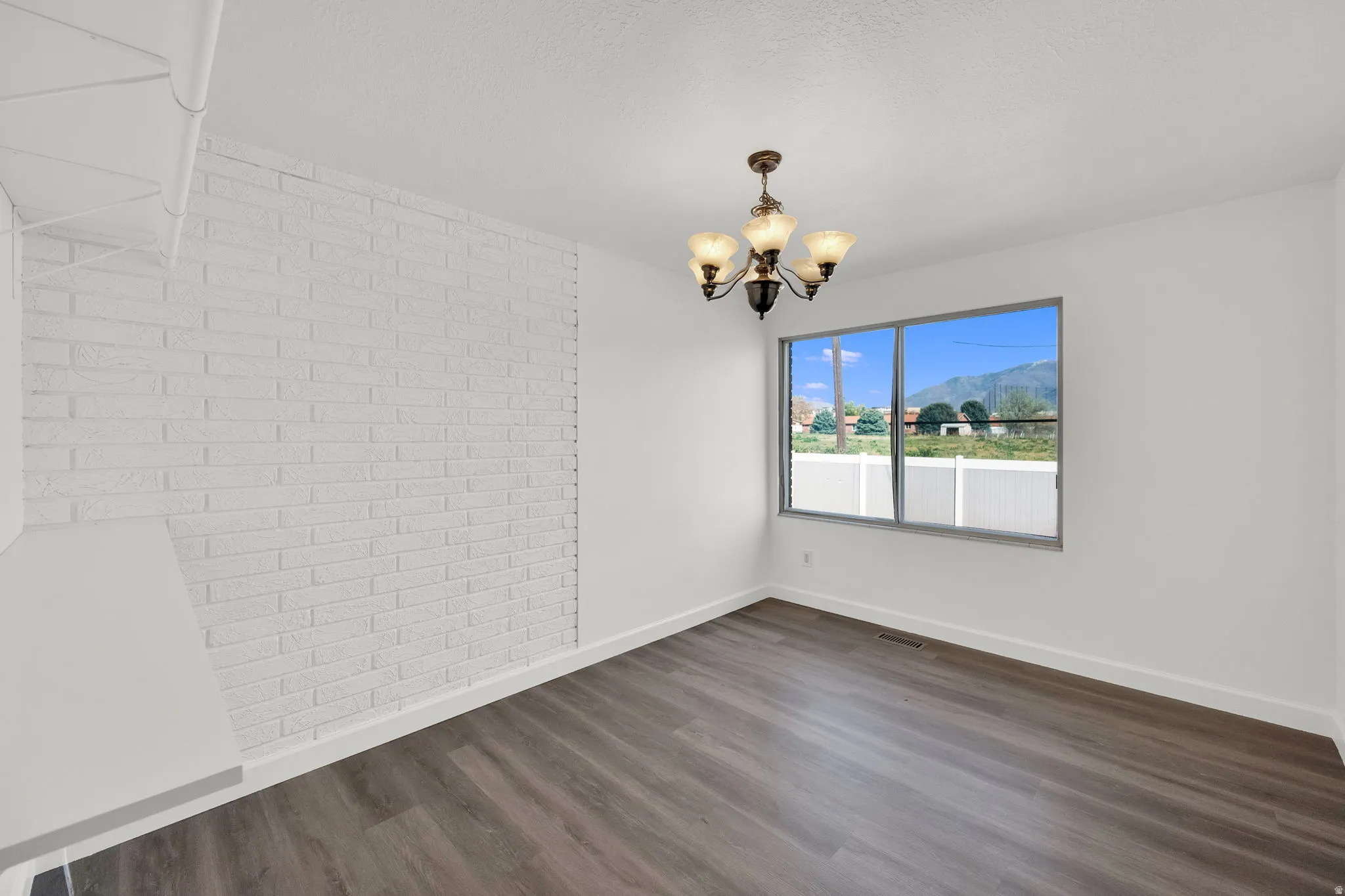 Unfurnished dining area with a mountain view, brick wall, dark wood-style floors, and a chandelier