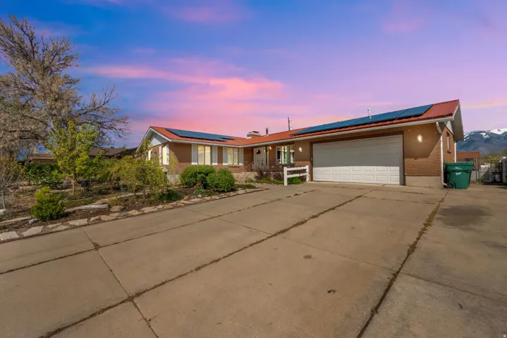 Ranch-style house with roof mounted solar panels, driveway, a garage, and a metal roof