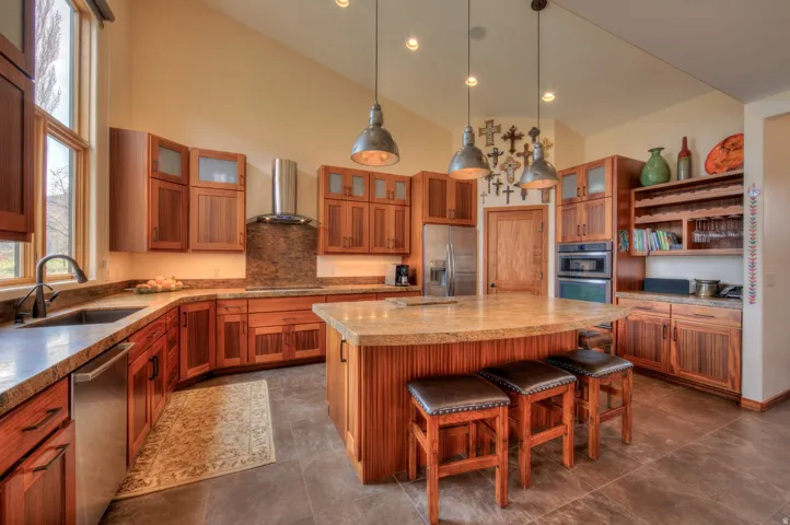 Kitchen with a breakfast bar, stainless steel appliances, pendant lighting, glass fronted cabinets, and vaulted ceiling