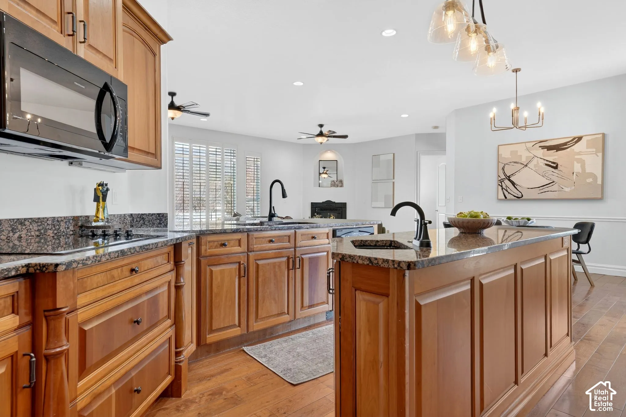 Kitchen with light wood-style flooring, black appliances, a peninsula, dark stone counters, and a warm lit fireplace